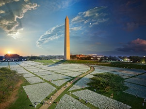 caption: A composite photograph captures the passage of day to night at the "In America: Remember" art installation on the National Mall in Washington, D.C. Each flag represents an American life lost to COVID-19.