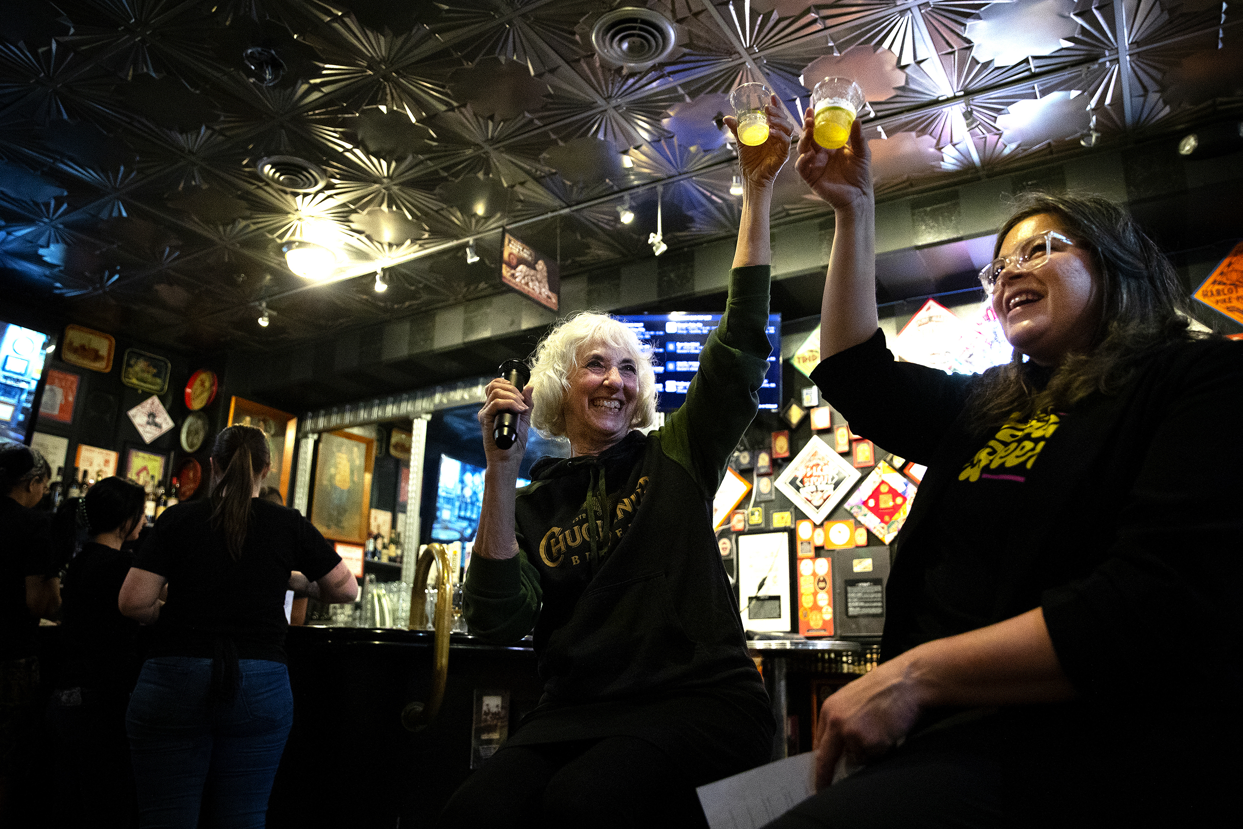 caption: Mari Kemper, left, and Leslie Shore, right, cheers after speaking to a crowd gathered to celebrate "Women in Beer," an annual fundraiser for the Rose Ann Finkel Diversity in Brewing Fund on Thursday, March 21, 2024, at the Pike Brewing Company in Seattle. 
