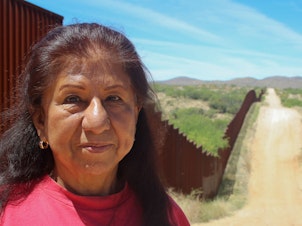 caption: Maria Ochoa poses by the Arizona-Mexico border wall, south of Tucson, Ariz.
