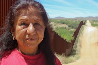 caption: Maria Ochoa poses by the Arizona-Mexico border wall, south of Tucson, Ariz.