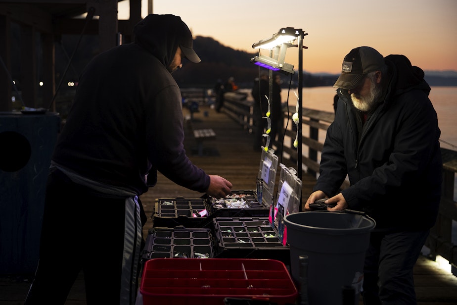 caption: Shawn Lindsey, left, purchases glow in the dark jigs for squidding from Curtis Alm, right, on Friday, Nov. 17, 2023, at Les Davis Pier in Tacoma. 