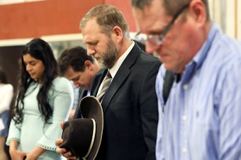 caption: Libertarian activist Ammon Bundy (second from right) prays during an Easter Sunday church service he organized despite concerns over the coronavirus outbreak in Emmett, Idaho.
