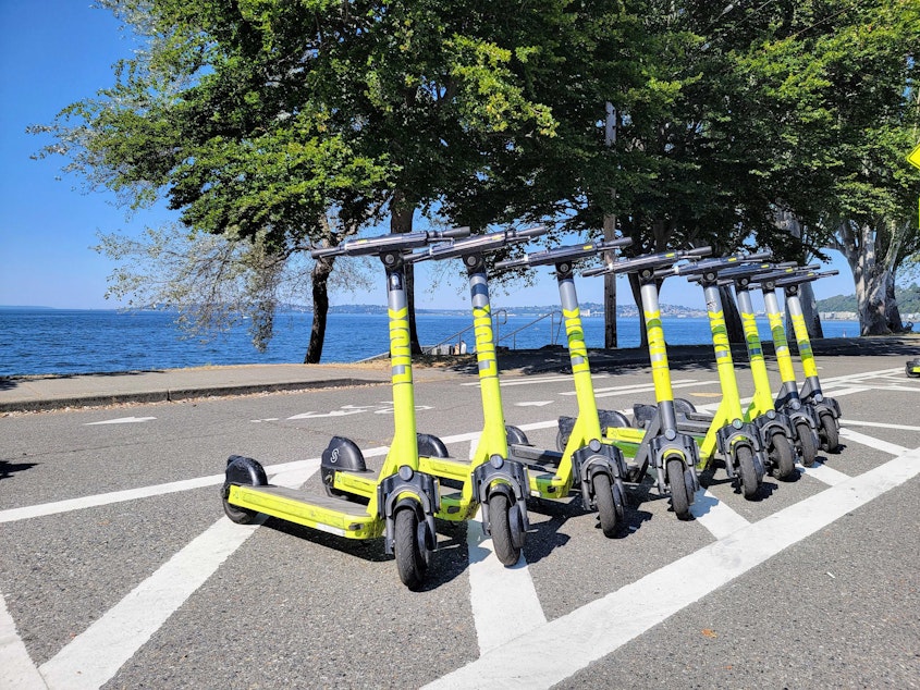 caption: A row of parked LINK scooters next to Alki Beach in West Seattle on July 28, 2022.