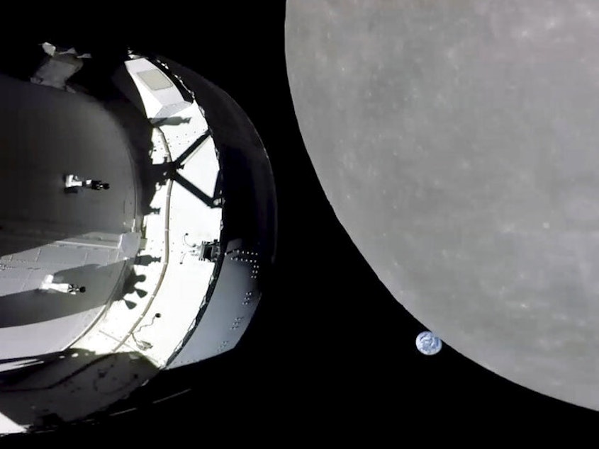 caption: This screengrab from NASA TV shows NASA's Orion capsule, left, nearing the moon, right, on Monday. At center is Earth.