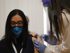 caption: A doctor receives Chicago's first COVID-19 vaccination on Tuesday. In a new poll released the same day, respondents appeared to show less reluctance to receiving a coronavirus vaccine.