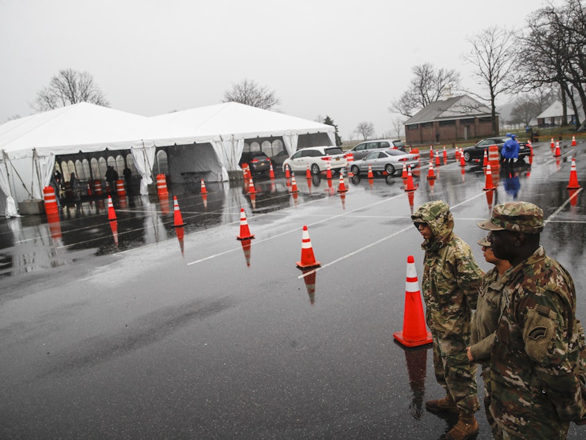 caption: National Guard personnel stand beside a line of motorists waiting for coronavirus testing in New Rochelle, N.Y., on Friday. Major retailers such as CVS, Target and Walmart are pledging to set up drive- through test sites in some of their parking lots.