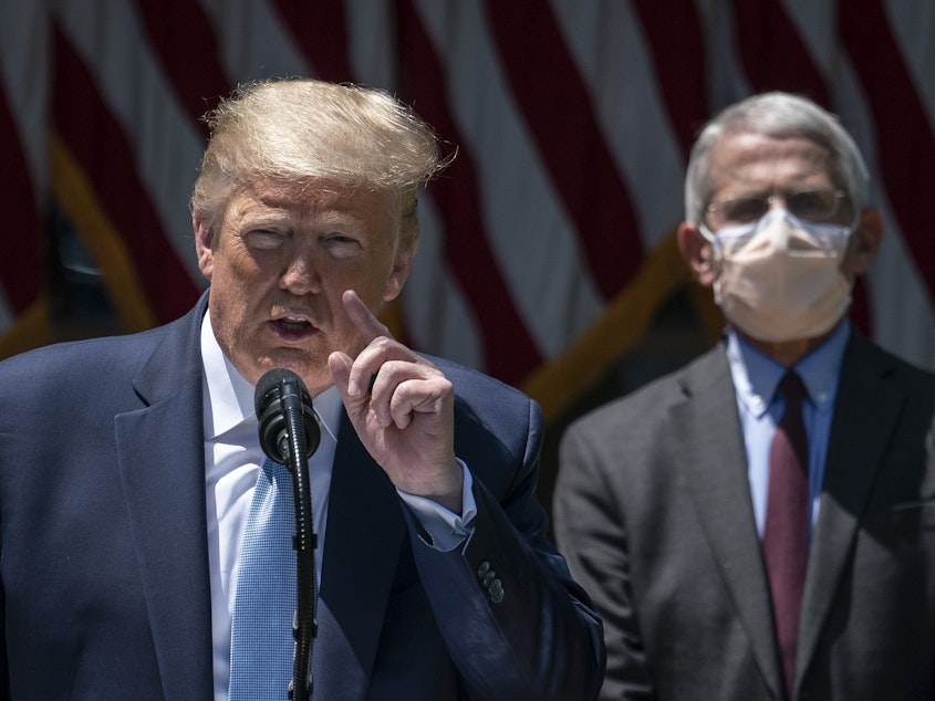 caption: WASHINGTON, DC - MAY 15: A masked Dr. Anthony Fauci looks on as President Trump delivers remarks about coronavirus vaccine development.