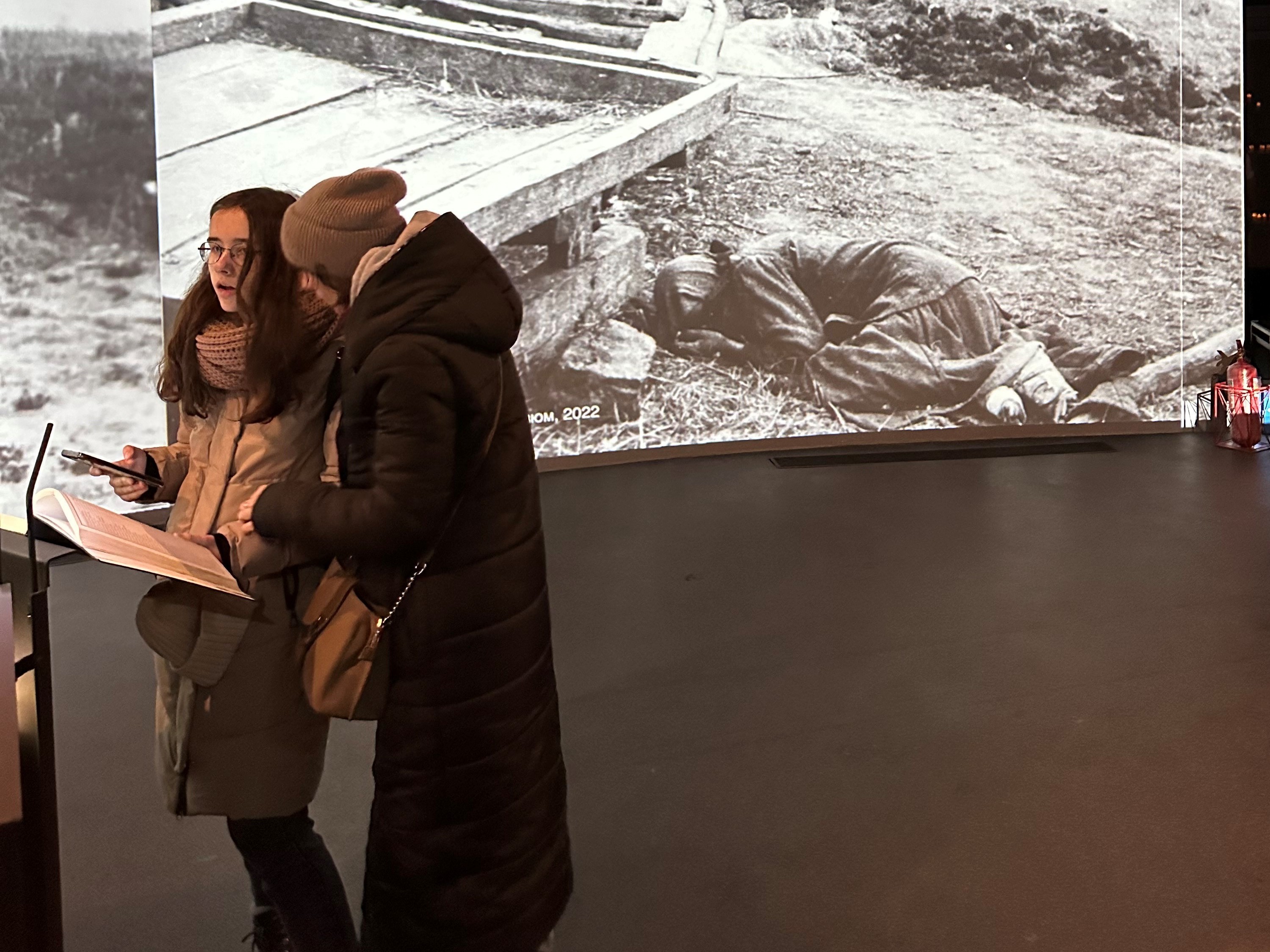 caption: Ukraine last month marked the 90th anniversary of a 1932-33 famine that the country blames on Soviet dictator Josef Stalin. In this photo, visitors to the National Museum of the Holodomor Genocide in Kyiv look though a book with some of the names of the 4 million or more Ukrainians who died in the famine. In the background is a photo of one of the victims of that period.