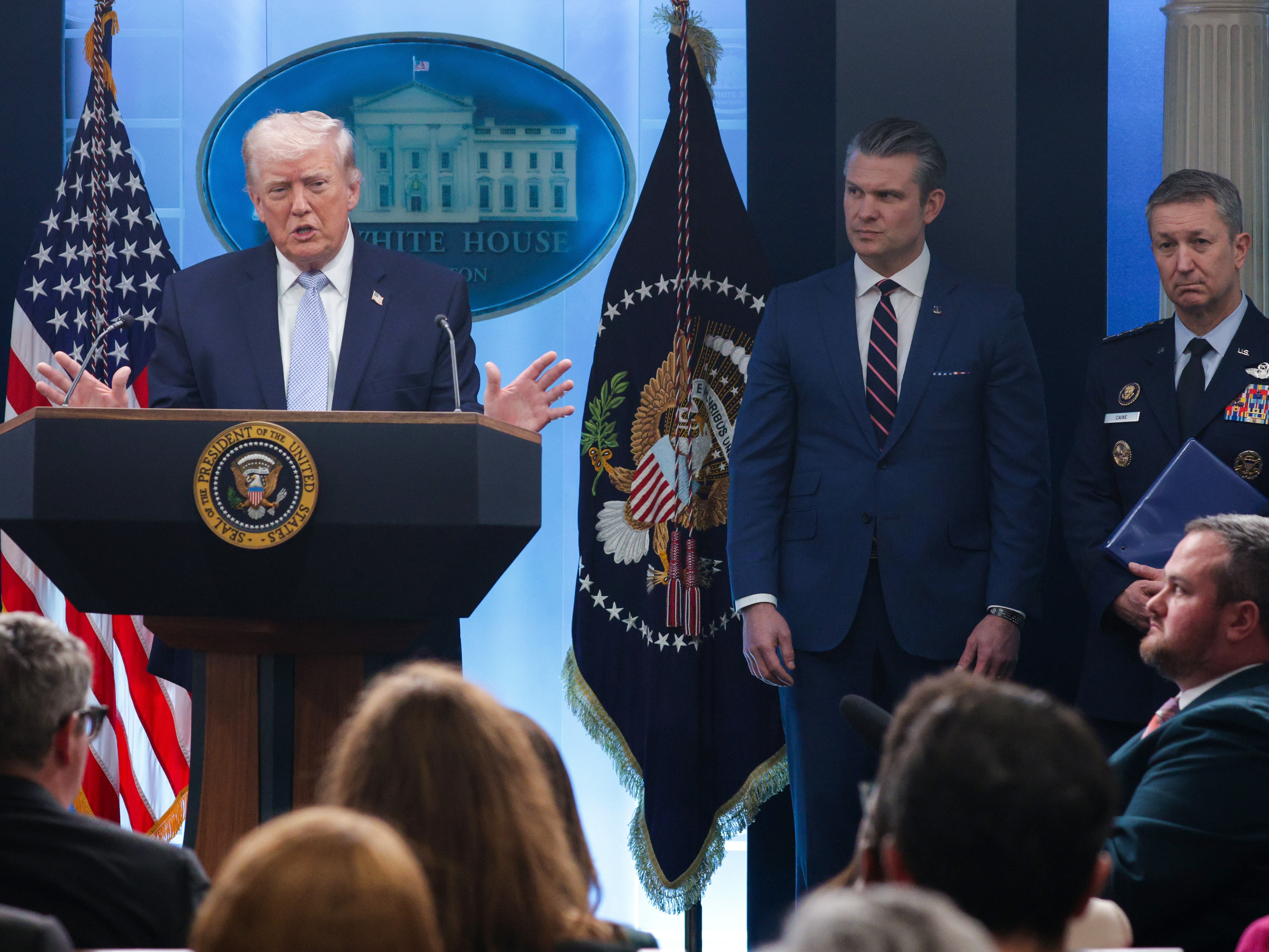 caption: President Trump speaks as Secretary of Defense Pete Hegseth  (center) and Chairman of the Joint Chiefs of Staff General Dan Caine look on during a news conference at the White House on April 6.