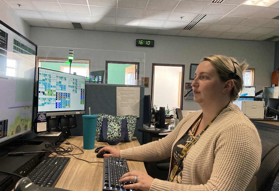 caption: Kayla White, a Washington State Patrol dispatcher, sits at her console in the Tacoma communications office. Most weeks she works three 12-hour days, in addition to two other regular 8-hour days, to make up for the ongoing staff shortages. In addition, she and her colleagues are now handling calls east of the Cascades after the Wenatchee communications center closed for lack of staff.