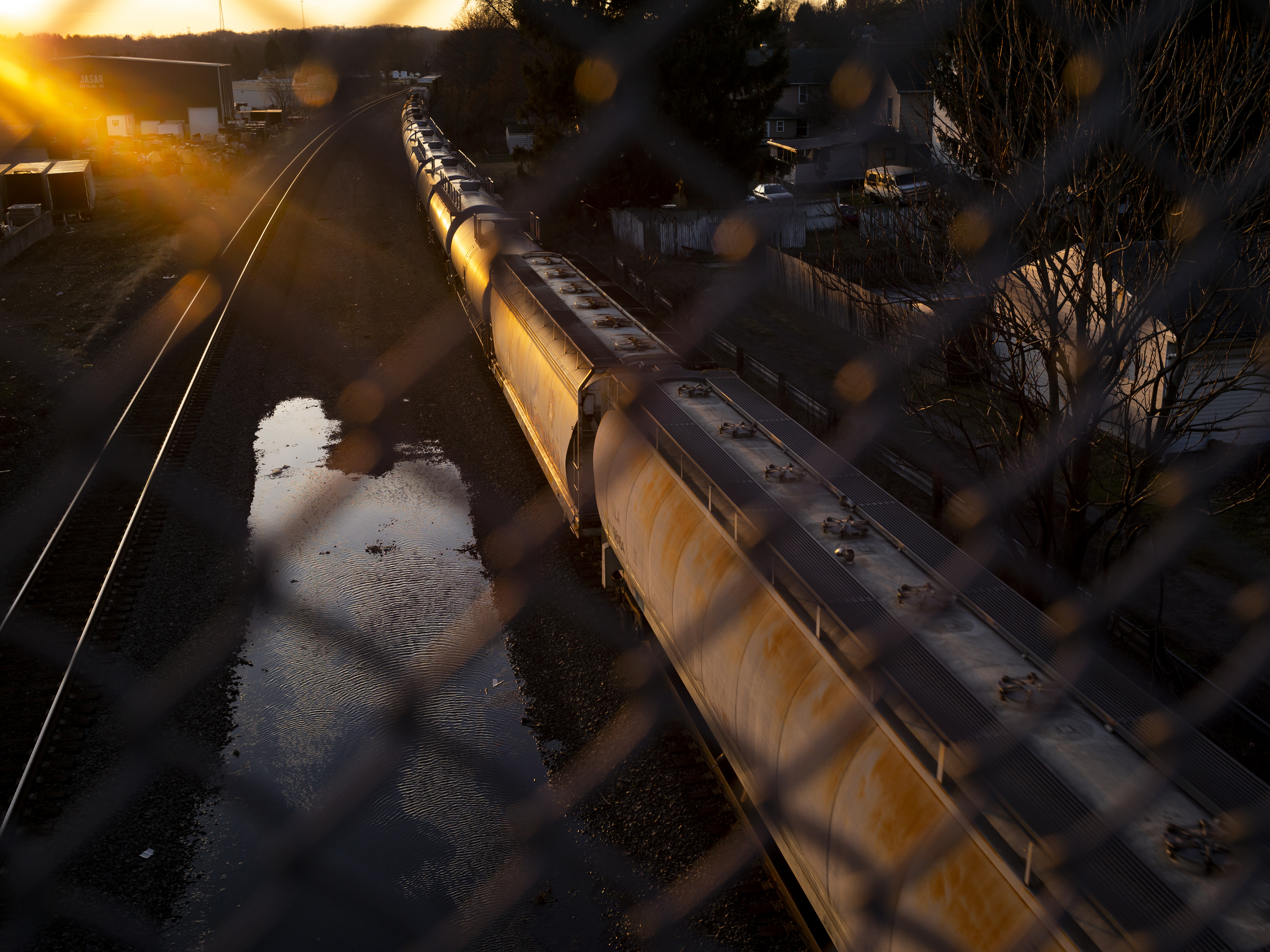 caption: A Norfolk Southern train passes underneath a bridge in East Palestine, Ohio, several weeks after a derailment spilled hazardous chemicals into the area's soil and water.