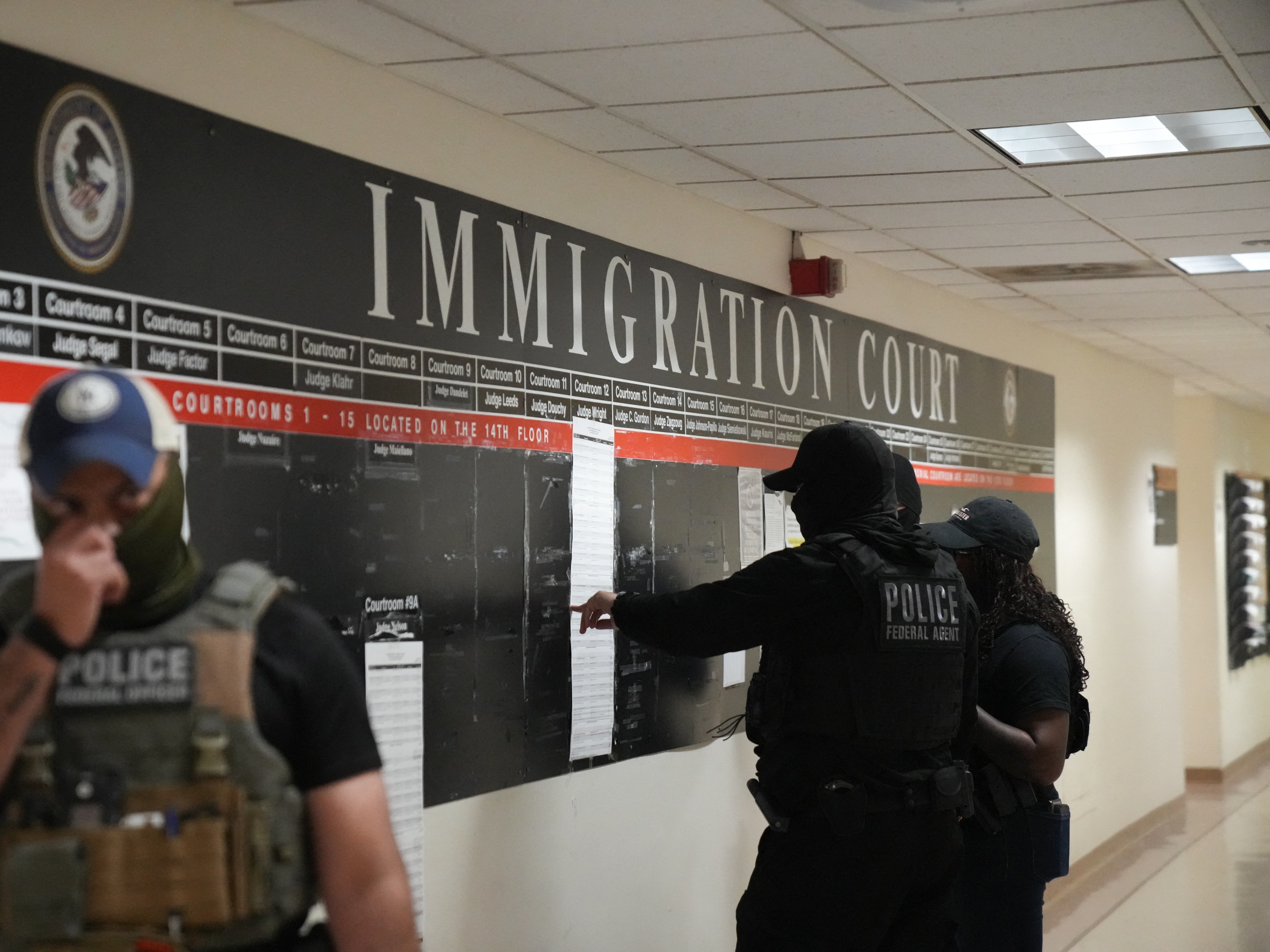 caption: U.S. Immigration and Customs Enforcement agents look over lists of names and their hearing times and locations inside the Federal Plaza courthouse in June 2025 in New York.