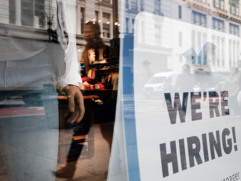 caption: People walk by a hiring sign in a store window in New York on Nov. 17.
