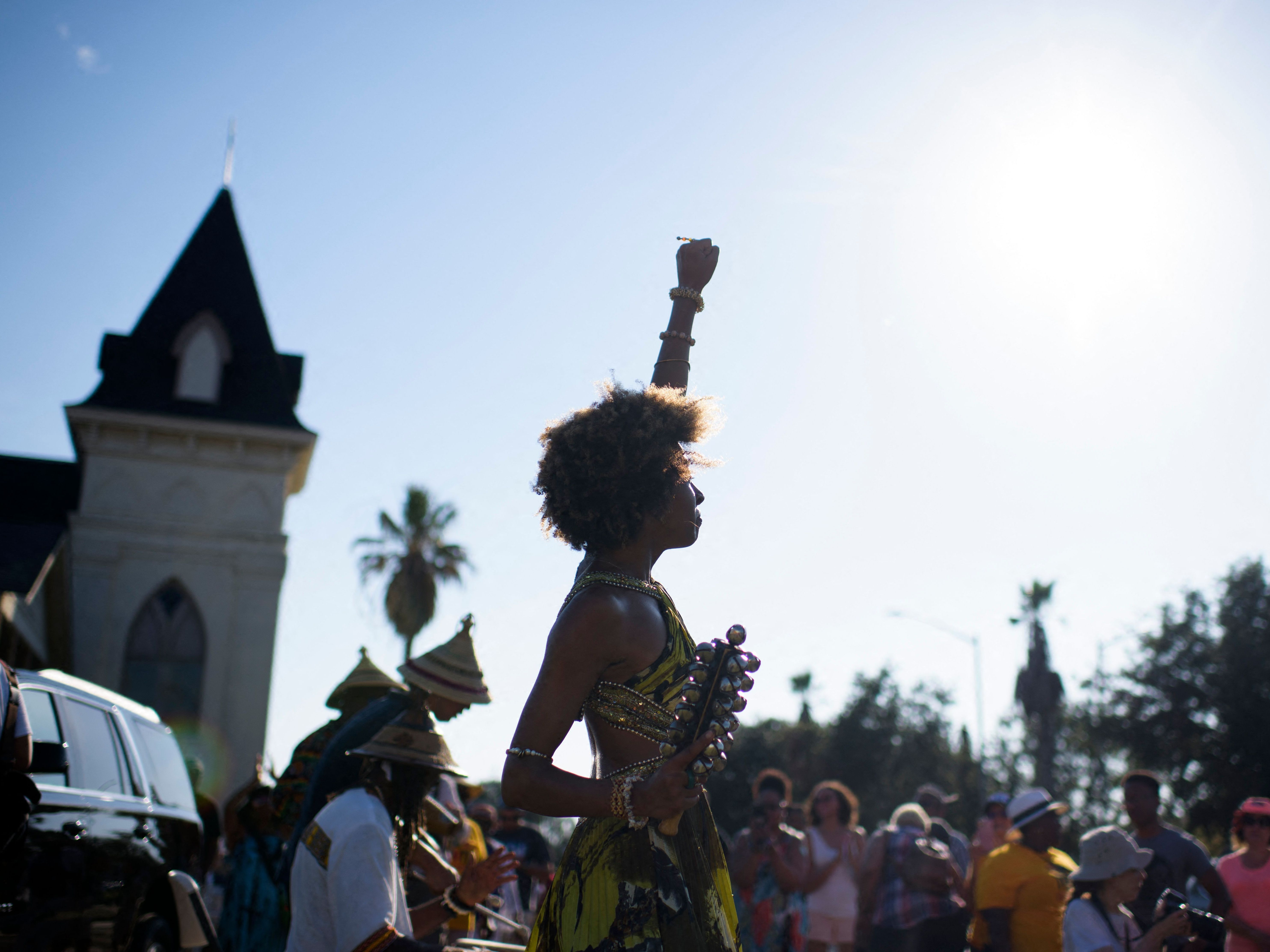 caption: Prescylia Mae raises her fist in the air during a Juneteenth re-enactment celebration in Galveston, Texas, on June 19, 2021.