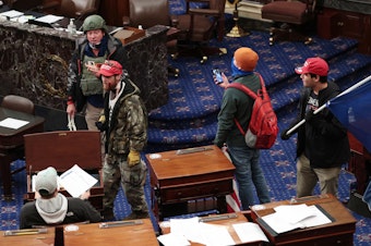 caption: Larry Rendall Brock Jr., an Air Force veteran, is seen inside the Senate Chamber wearing a military-style helmet and tactical vest during the rioting at the U.S. Capitol. Federal prosecutors have alleged that before the attack, Brock posted on Facebook about an impending "Second Civil War."