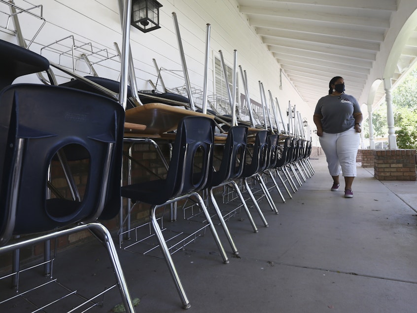 caption: Kristina Washington, special education staff member at Desert Heights Preparatory Academy, walks past desks and chairs at the closed Glendale, Ariz., school in early June.