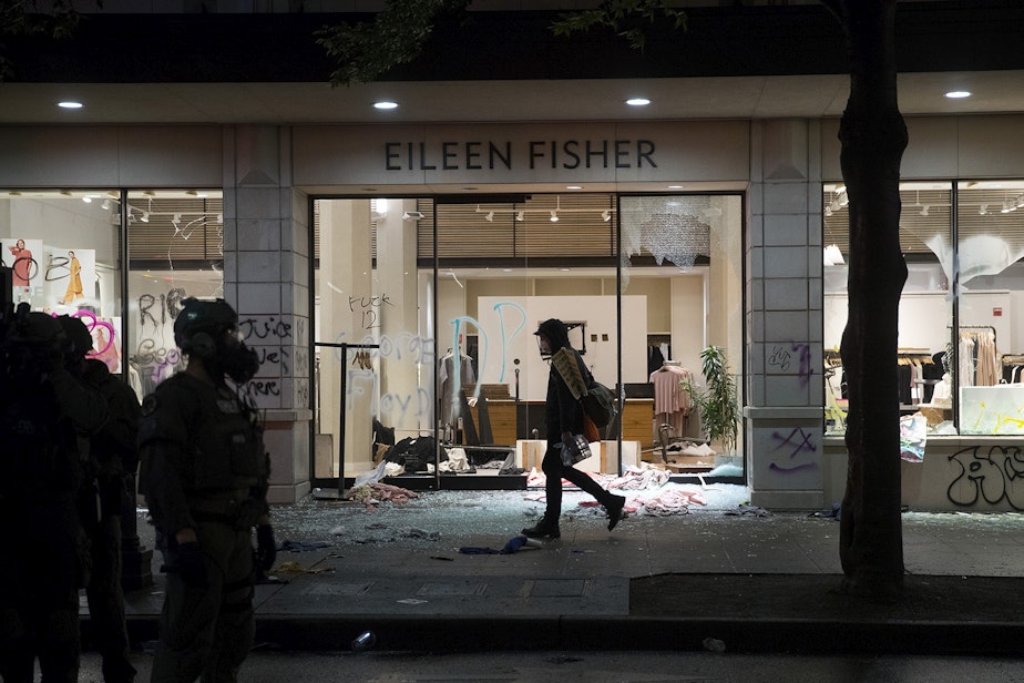 caption: A protester walks in front of an Eileen Fisher store that was damaged following a protest that turned chaotic on Saturday, May 30, 2020, in Seattle. Protesters gathered to express outrage at the violent police killing of George Floyd, a Black man who was killed by a white police officer who held his knee on Floyd's neck for 8 minutes and 46 seconds, as he repeatedly said, 'I can't breathe,' in Minneapolis on Memorial Day.