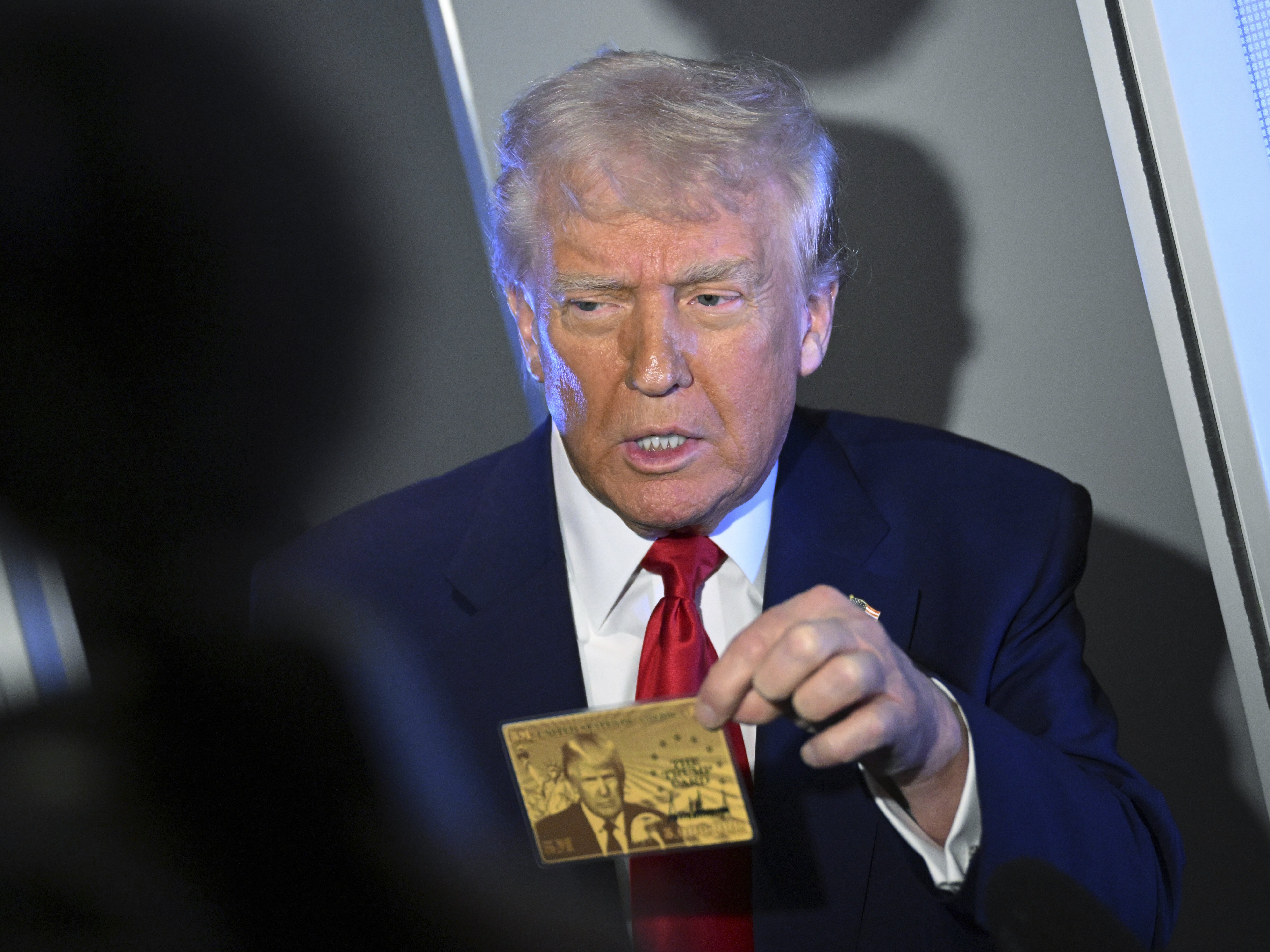 caption: President Donald Trump holds up the $5 million gold card as he speaks to reporters while in flight on board Air Force One, en route to Miami, Thursday, April 3, 2025.