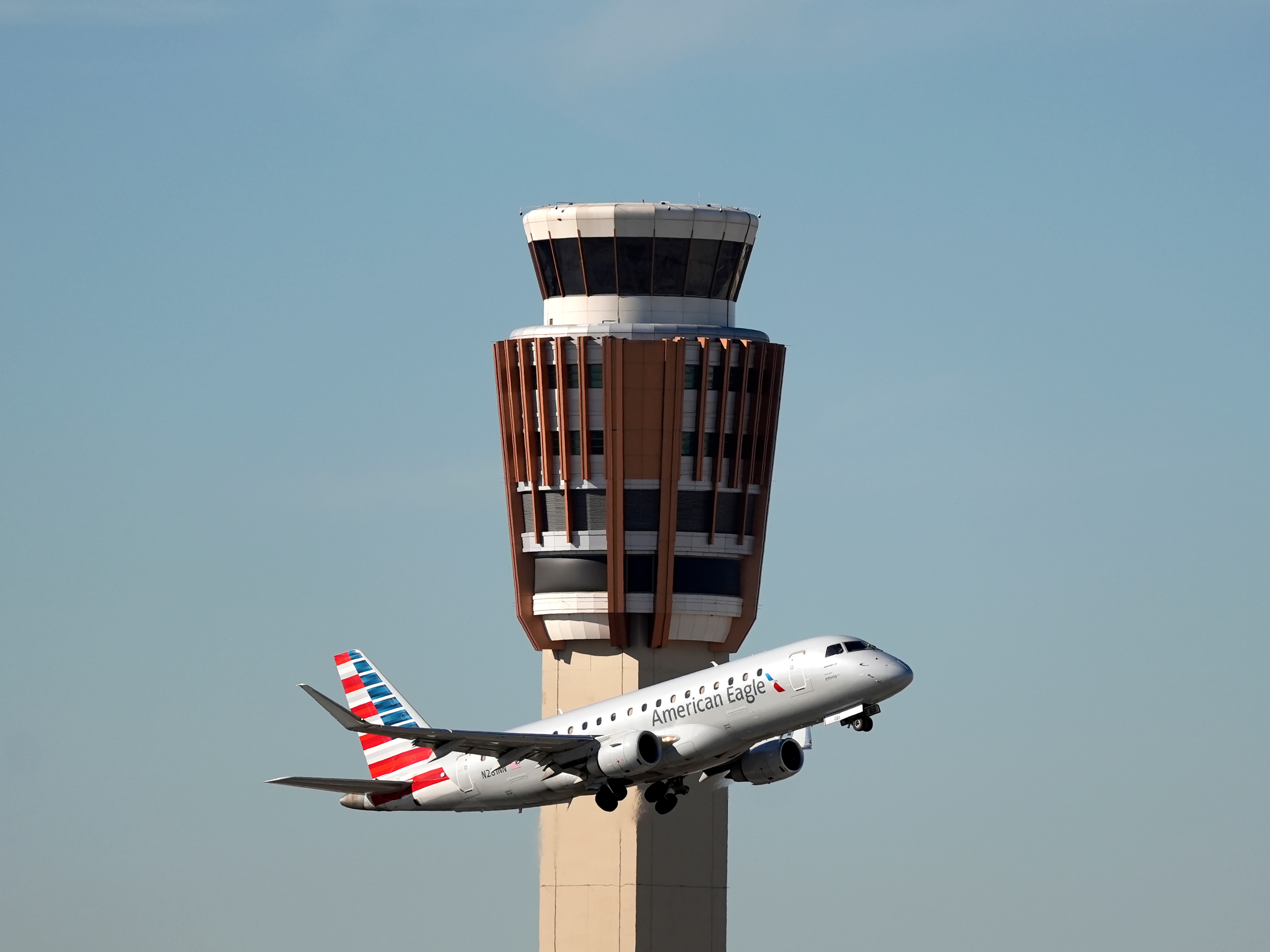 caption: An American Eagle jet flies past the air traffic control tower at Phoenix Sky Harbor International Airport on, Nov. 8, 2025. As essential employees, controllers were required to work during the government shutdown without pay. When the last shutdown ended in 2019, it took some years to get all the money they were owed.