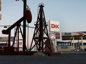 caption: A statue of a pumpjack and drilling rig sits next to a gas station in Odessa, Texas, on March 13. U.S. oil companies are under pressure to drill more, but they are constrained in how much they can do.