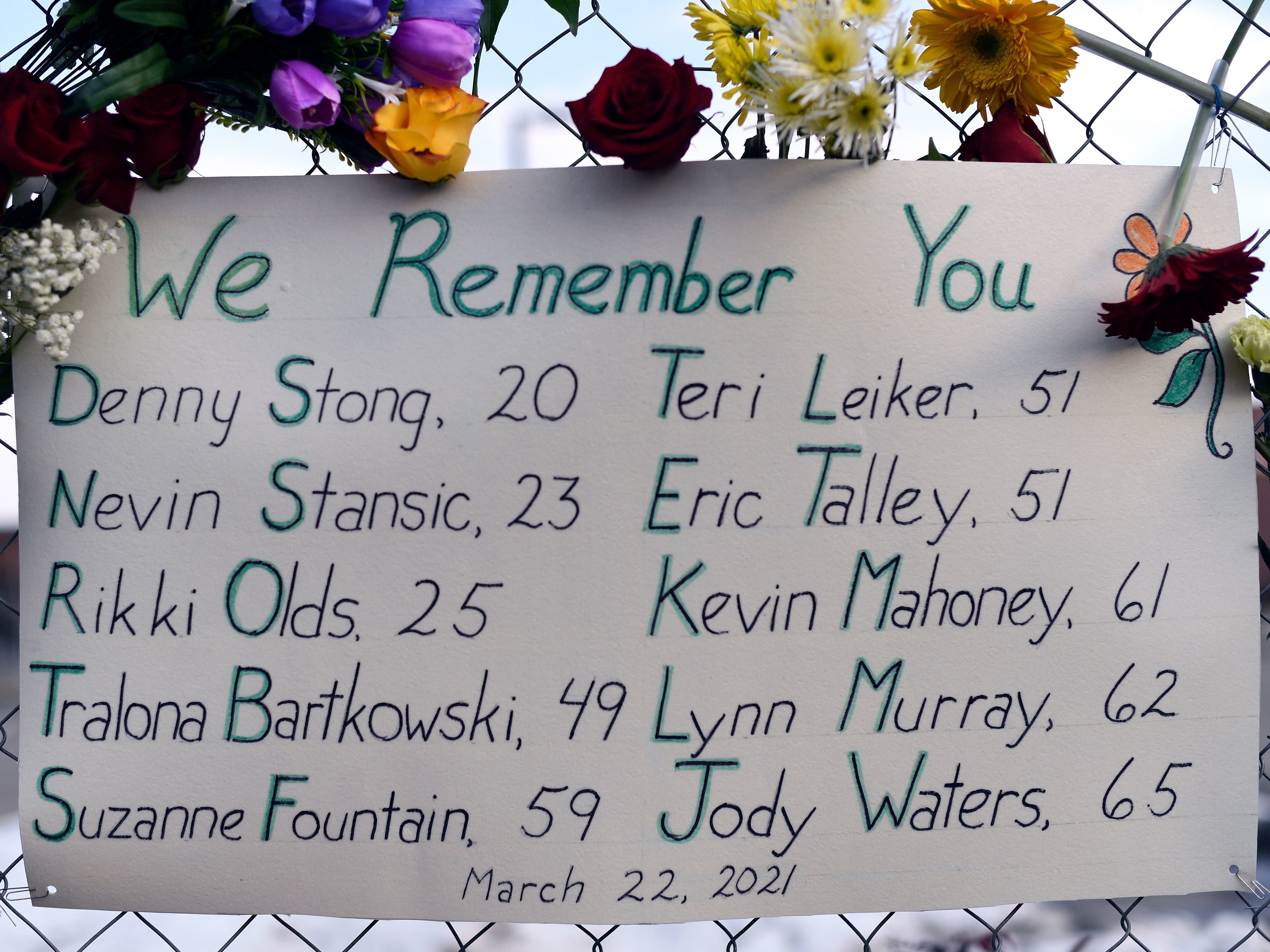 caption: A sign framed with flowers lists the victims' names on the fence outside a King Soopers grocery store in Boulder, Colo. The suspected gunman is making his first court appearance on Thursday.