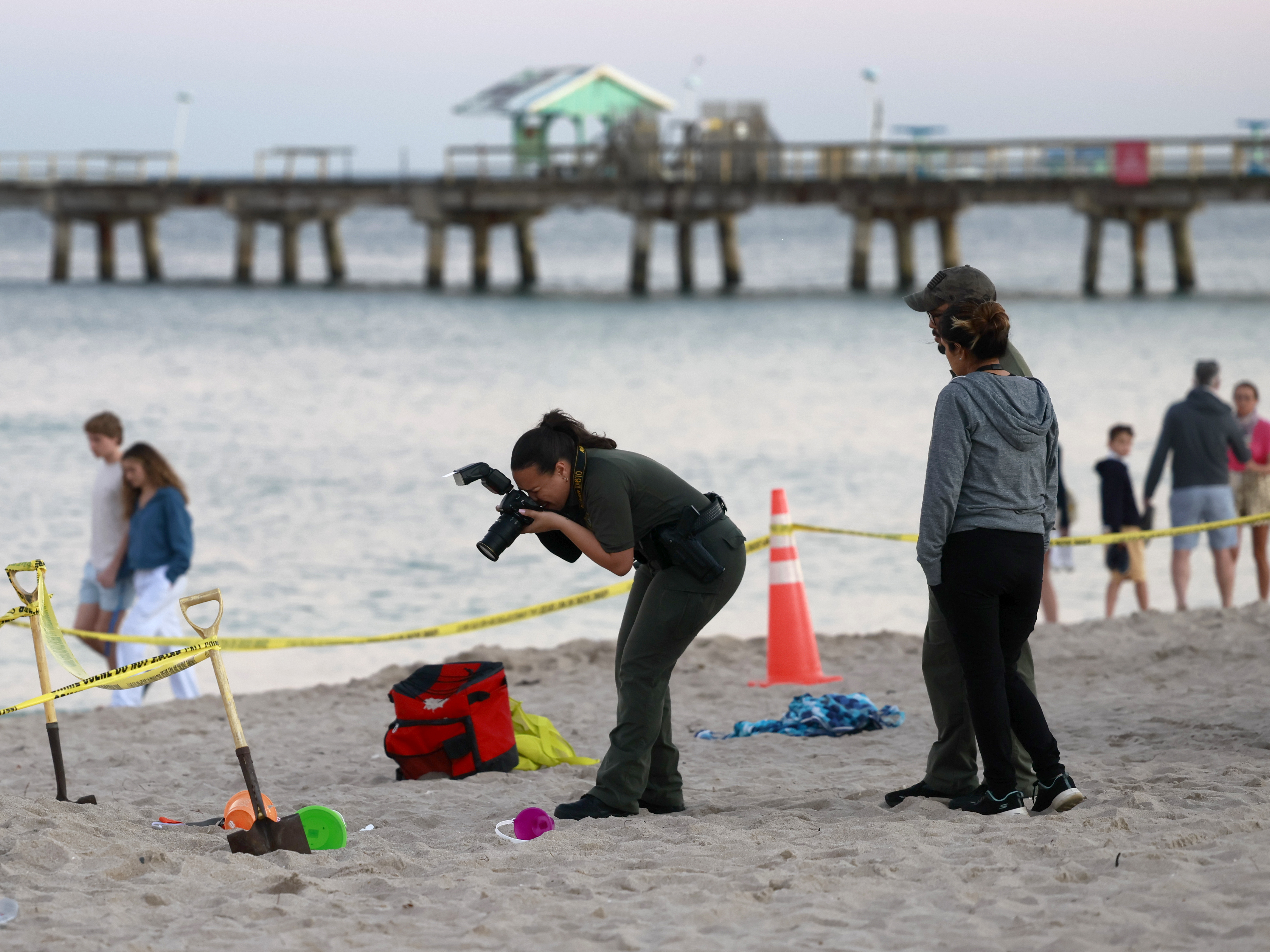 caption: Investigators on the beach in Lauderdale-by-the-Sea, Fla., take photos of the scene of a sand collapse on Tuesday, Feb. 20, 2024.