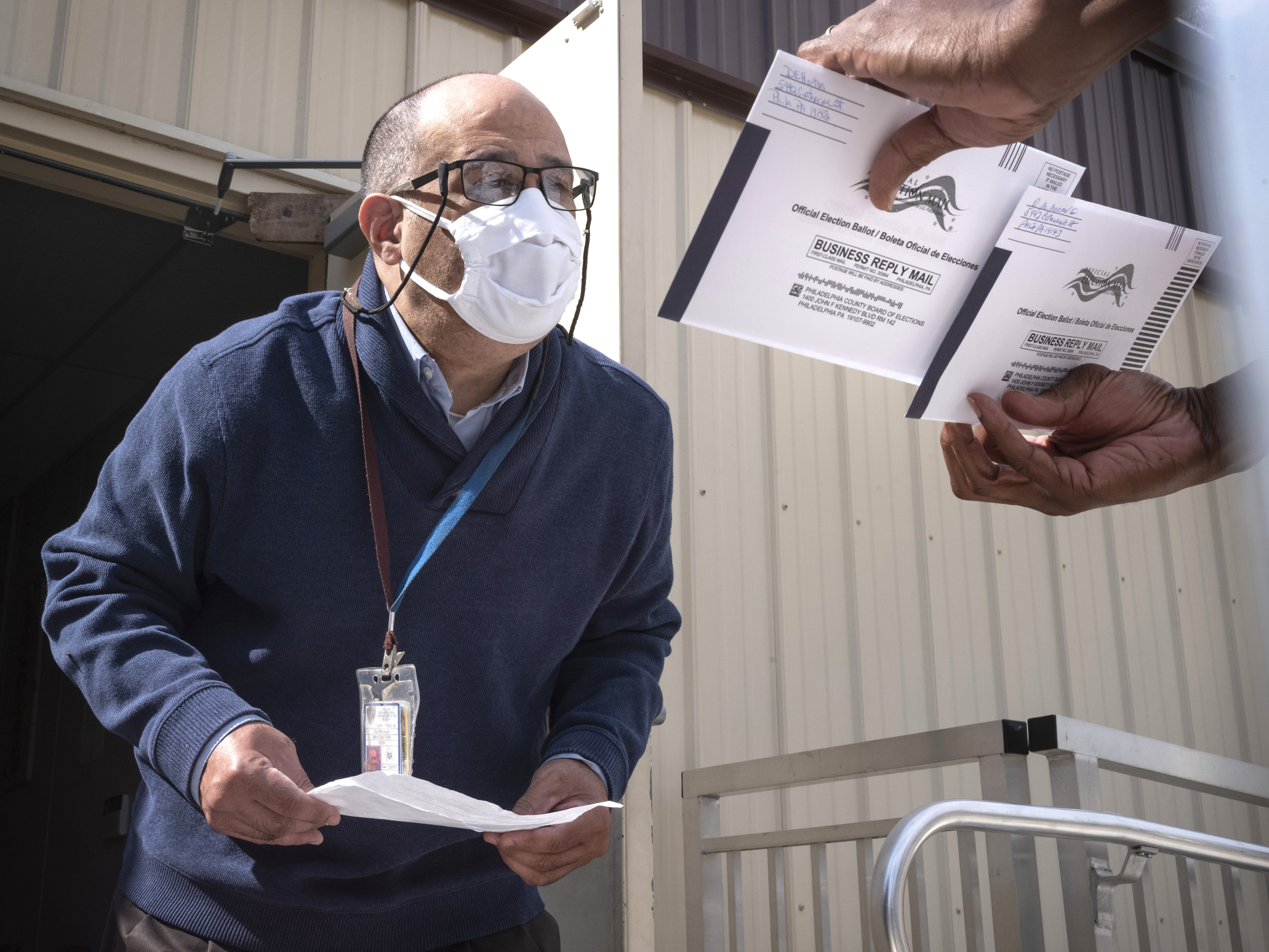 caption: An employee of the Philadelphia City Commissioners Office examines ballot envelopes at a satellite election office at Overbrook High School in Philadelphia. Local election clerks can't start verifying mailed-in ballots in Pennsylvania until Election Day and in Michigan until the day before.