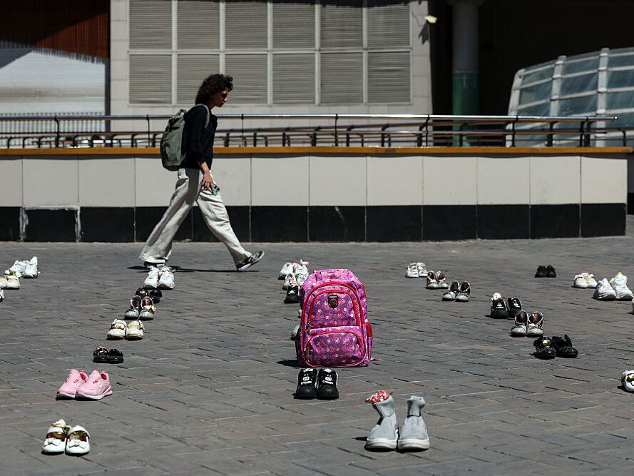 caption: An Iranian woman walks past symbolic belongings laid on the ground at Valiasr Square in Tehran on April 24, 2026, in tribute to the schoolgirls in Minab killed in an airstrike.