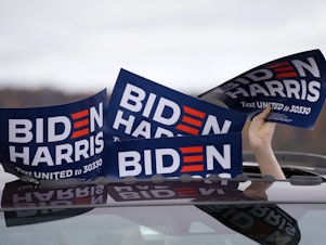 caption: A person holds signs from the sunroof of a vehicle during a campaign event for Joe Biden.