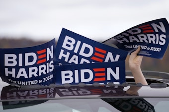caption: A person holds signs from the sunroof of a vehicle during a campaign event for Joe Biden.