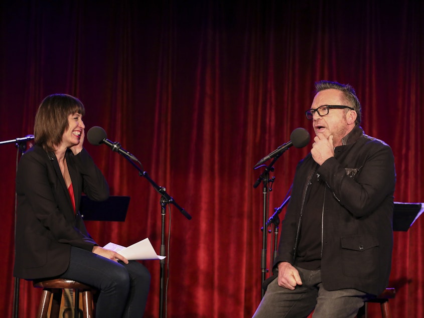 caption: Ophira Eisenberg chats with Tom Arnold on <em>Ask Me Another</em> at the Bell House in Brooklyn, New York.