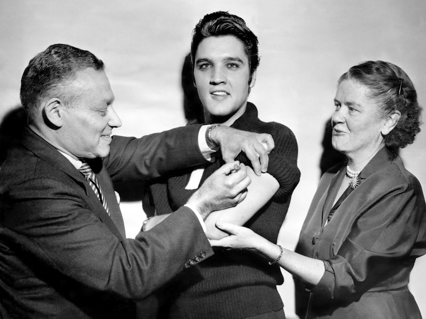 caption: Elvis Presley got his polio vaccination from Dr. Harold Fuerst and Dr. Leona Baumgartner at CBS' Studio 50 in New York City on Oct. 28, 1956. The chart-topping singer took part in a March of Dimes campaign to convince teens to get vaccinated.