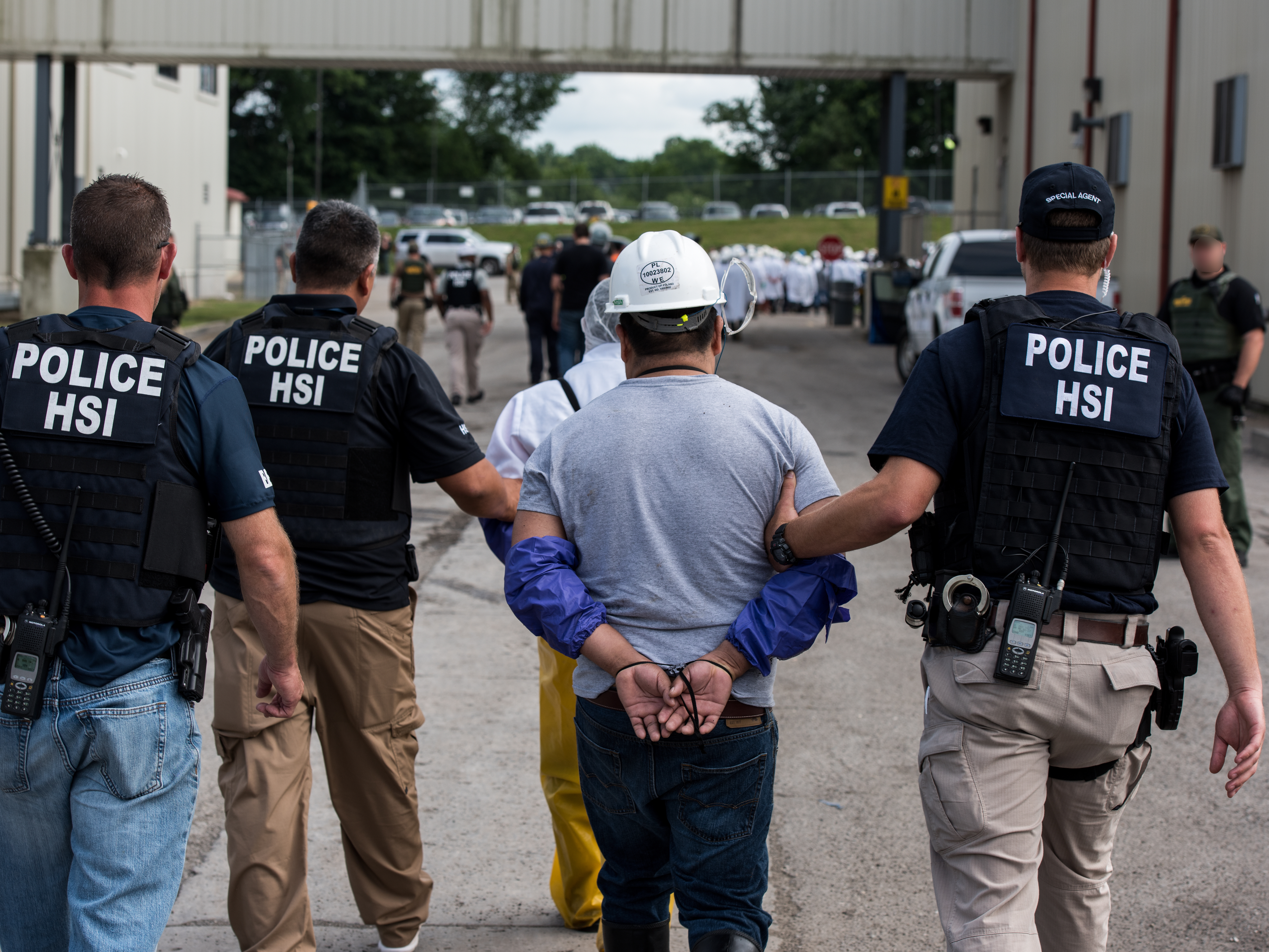 caption: "We will not tolerate unscrupulous employers who exploit unauthorized workers," Homeland Security Secretary Alejandro Mayorkas said, as he ordered a halt to mass workplace raids. Here, special agents with Homeland Security Investigations lead a worker away from a workplace raid in Ohio in 2018, part of a string of such operations during the Trump administration.
