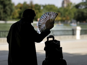 caption: A man uses a hand fan in a park in central Madrid during a heat wave.