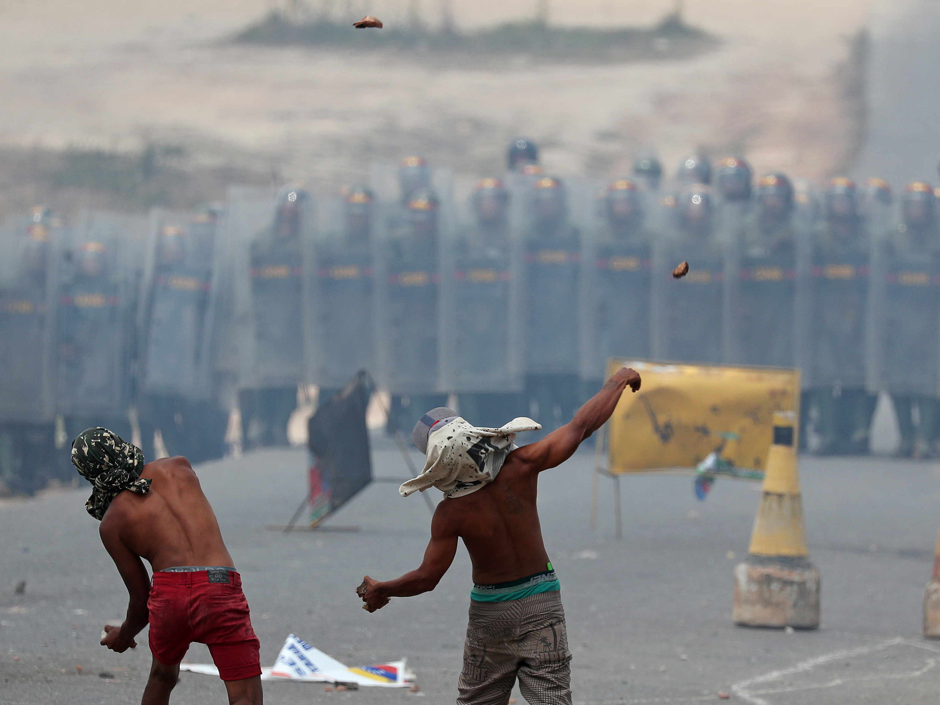 caption: Demonstrators throw stones at a line of Venezuelan National Guard troops along Venezuela's border with Brazil, at the Brazilian city of Pacaraima on Sunday.