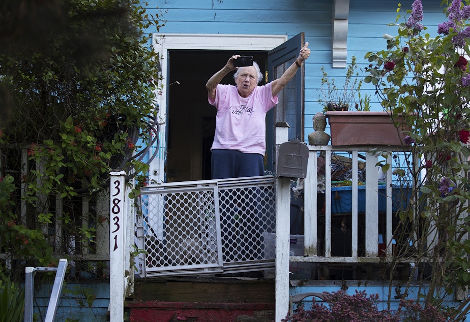 caption: A Wallingford resident cheers and gives a thumbs up for the Seattle Quarantine Parade as it drives through the neighborhood on Friday, May 8, 2020, in Seattle. 