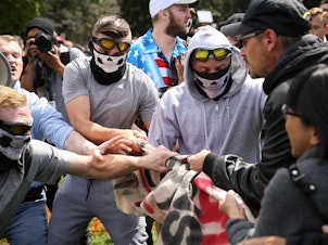 caption: Rise Above Movement members wearing their skeleton masks pull away a counterprotester's flag at a Patriots Day rally last April in Berkeley, Calif. Four RAM members were arrested for violence at the rally and a string of others.