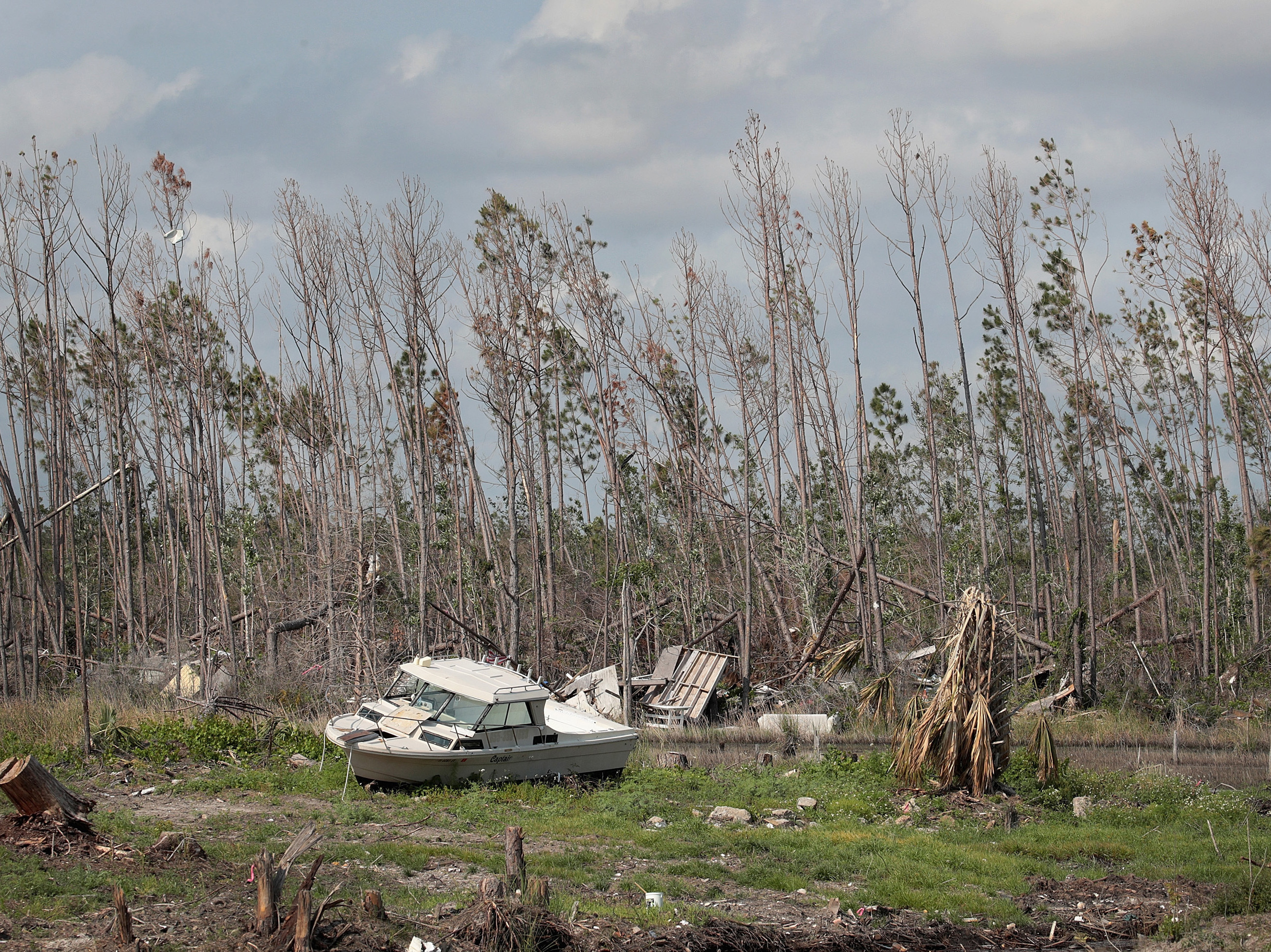 caption: A boat carried by Hurricane Michael rests along a tree line near a canal in May in Mexico Beach, Fla. Seven months after the Category 5 hurricane made landfall near the small community, the town is still littered with heavily damaged and destroyed homes and businesses.