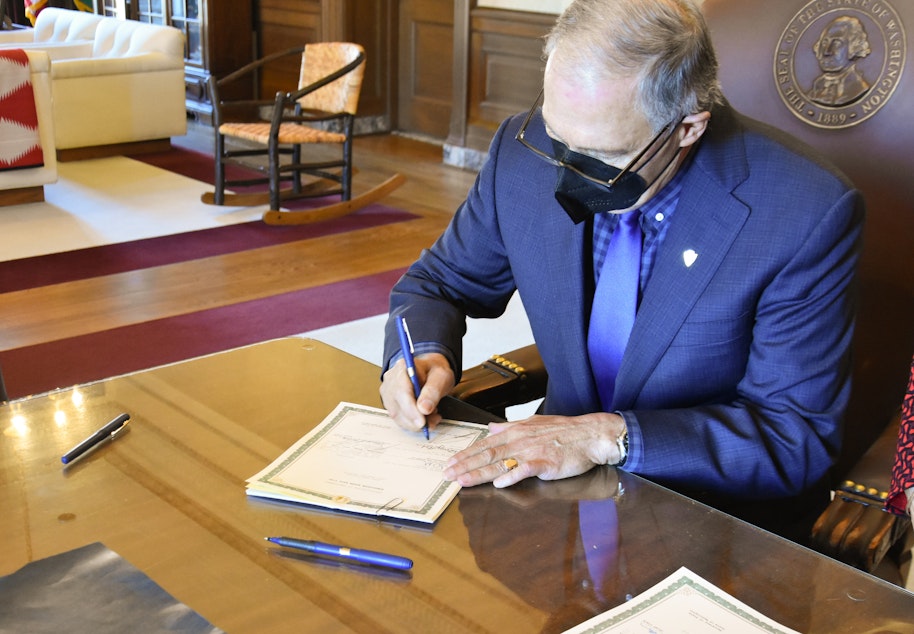 caption: Wash. Gov. Jay Inslee signs two bills into law on Jan. 27, 2022 that make changes to the state's first-in-the-nation long-term care program known as WA Cares.