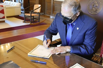 caption: Wash. Gov. Jay Inslee signs two bills into law on Jan. 27, 2022 that make changes to the state's first-in-the-nation long-term care program known as WA Cares.