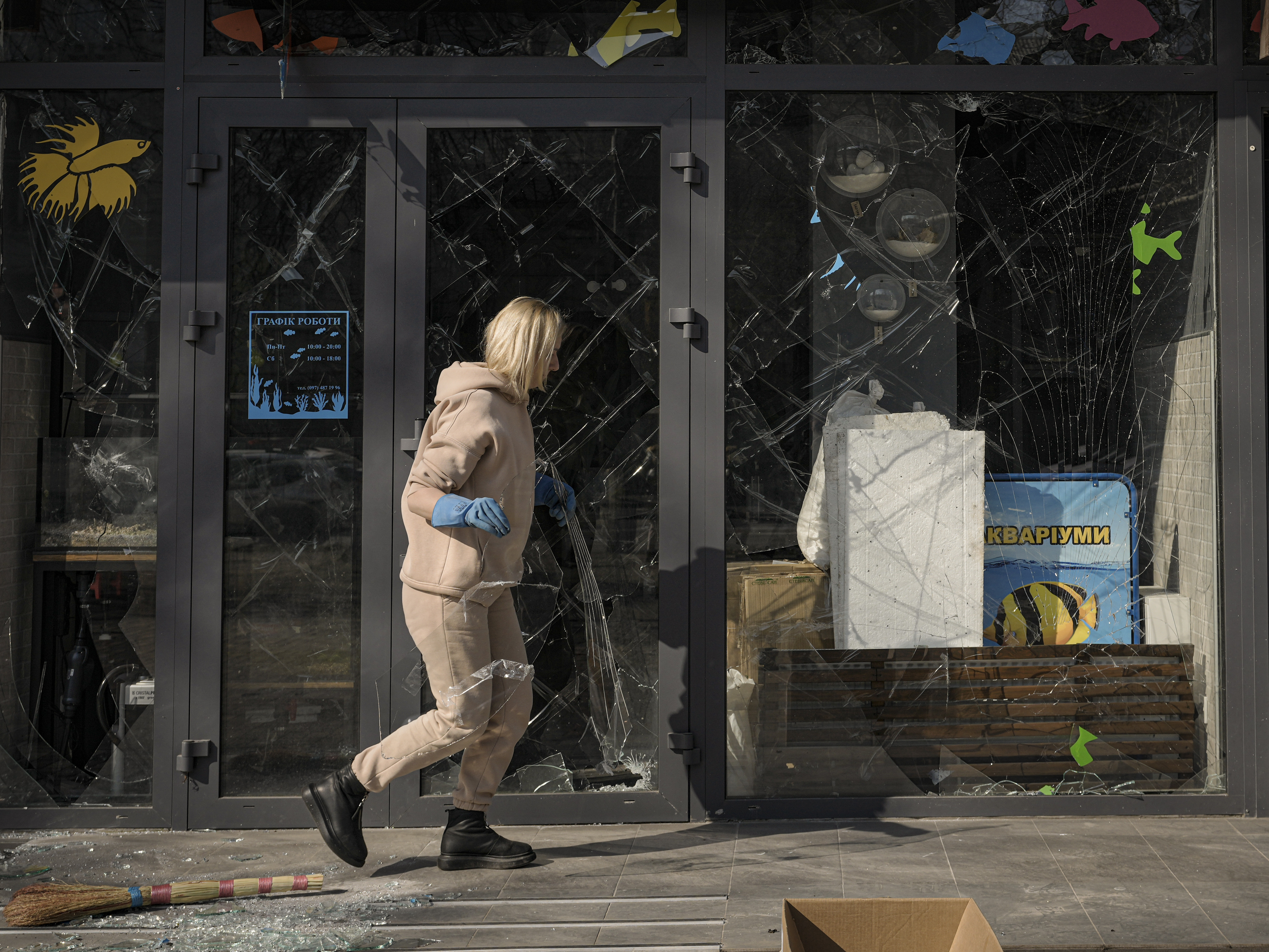 caption: A woman removes pieces of broken glass from a shop window after a bombing in Kyiv, Ukraine, on March 23.