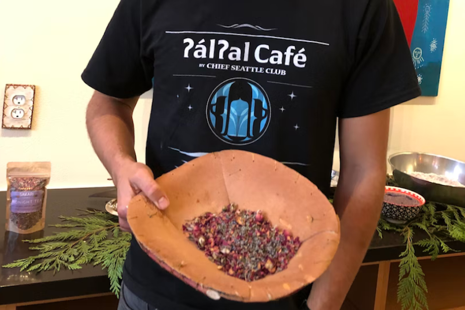 caption: Anthony Johnson (Anishnaabe) is manager and chef at ?al?al Café in Pioneer Square. The café is focused on Indigenous foods. Johnson is holding a bowl of midnight (herbal) tea from Oregon. 