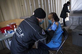 caption: Seattle Firefighter and EMT Dave Pedras, left, administers the first dose of the Moderna Covid-19 vaccine for Du, 87, on Thursday, February 18, 2021, at the West Seattle Covid-19 testing site on Southwest Thistle Street in Seattle. The pop-up vaccination clinic was set up for older Latino community members who were referred by El Comite or Villa Comunitaria.