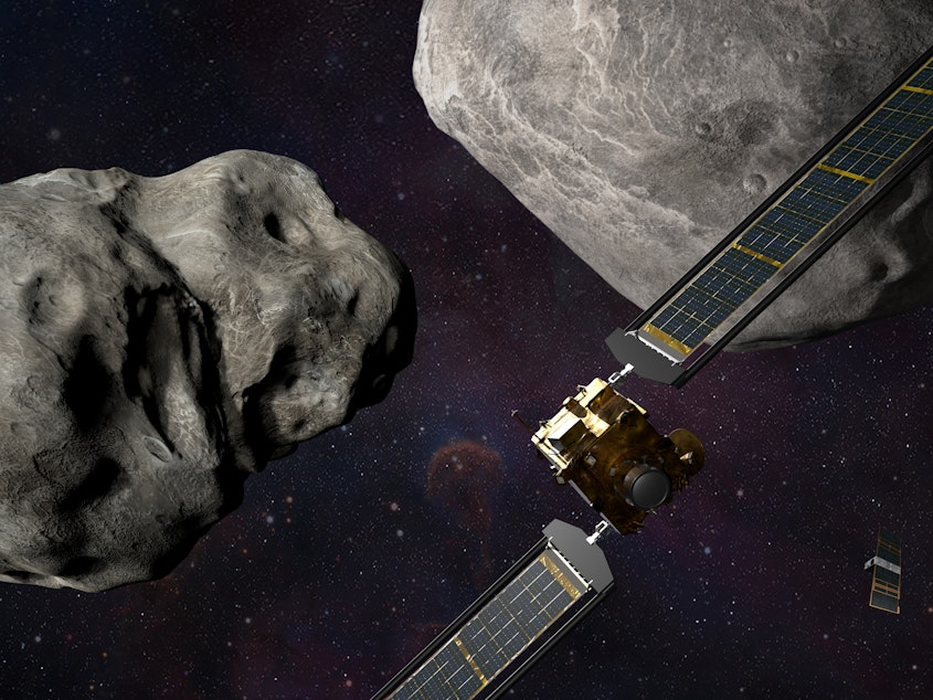 caption: This illustration shows the DART spacecraft approaching the two asteroids, Didymos and Dimorphos, with a small observing spacecraft nearby.