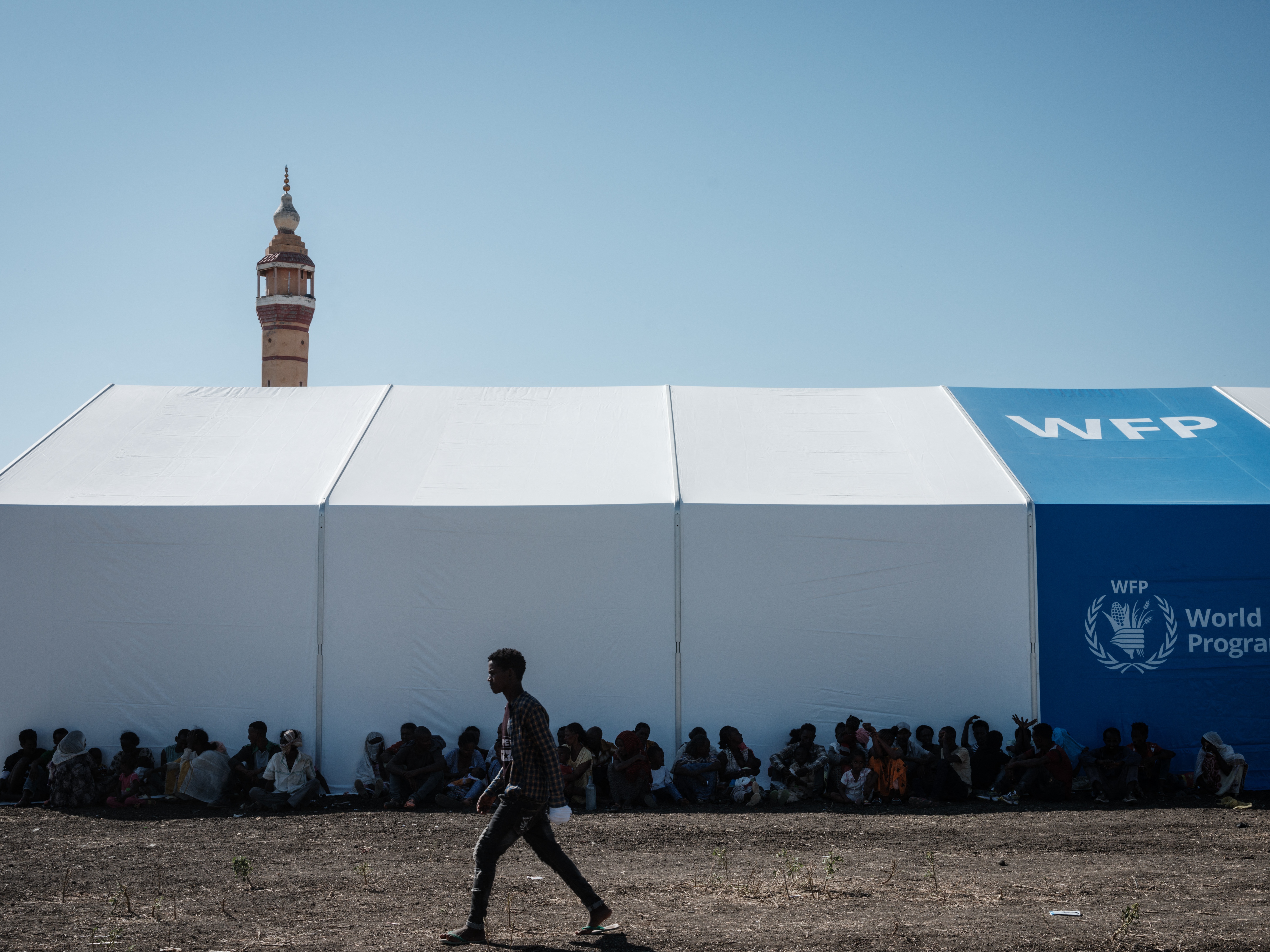 caption: Ethiopian refugees rest in the shadow of a warehouse erected by the World Food Programme near the Ethiopian border in Gedaref, eastern Sudan.