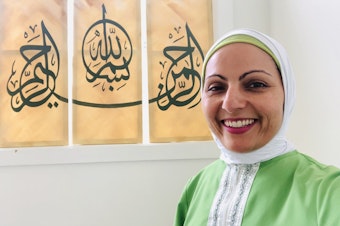 caption: Aneelah Afzali is the executive director of the American Muslim Empowerment Network, A program of the Muslim Association of Puget Sound. The writing behind her says "In the name of God, the Most Gracious, the Most Merciful."