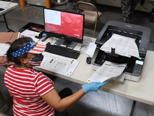 caption: A Clark County, Nev. election worker scans mail-in ballots on October 20, 2020 in North Las Vegas. Nevada allows officials to count ballots received in advance of Election Day in order to speed the tabulation of results that evening.