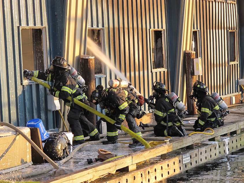 caption: Firefighters put out flames at the Salmon Bay Marina, one of three fires caused by spontaneous combustion this month.