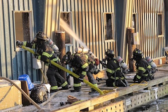 caption: Firefighters put out flames at the Salmon Bay Marina, one of three fires caused by spontaneous combustion this month.