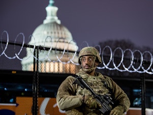 caption: A member of the Virginia National Guard stands outside the razor wire fencing surrounding the U.S. Capitol on Friday. Up to 25,000 troops are expected by Inauguration Day.